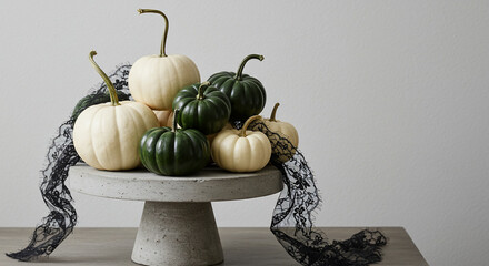 An arrangement of white and green pumpkins displayed on a gray concrete cake stand, accented with black lace.