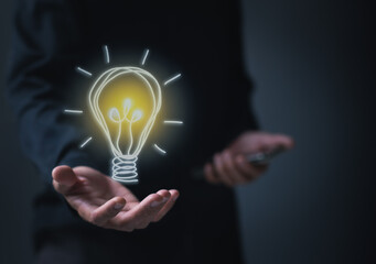 Hand holding a light bulb. Man holding glowing light bulb icon on black background. Ideas, innovations, ideas and inspiration for business ideas.