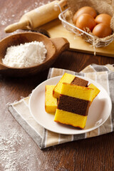 A white plate holds several slices of a rich Lapis Surabaya cake, with the rest of the cake and a cup of tea visible in the background