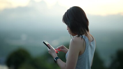 A young Asian woman, smiles brightly with closed eyes as she interacts with her smartphone outdoors. Dynamic CG overlays of Like and Heart emojis float around her. - Powered by Adobe