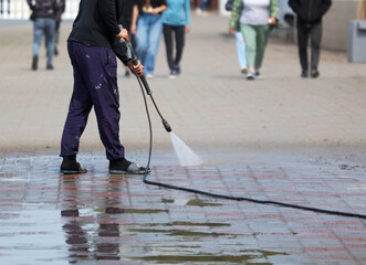 Obraz premium A man is cleaning a sidewalk with a pressure washer