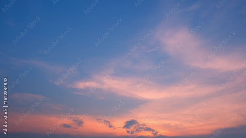 Wall mural a timelapse video captures a peaceful sunset sky where soft pink and orange clouds gently float acro