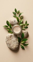 Light beige jar of cream sits atop stones, surrounded by fresh green leaves on a pale background