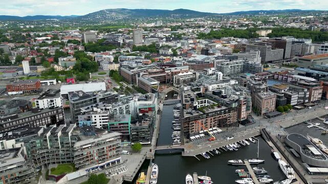 Aerial view of the modern Aker Brygge waterfront lined with colorful buildings and boats docked in the harbor contrasting with the city beyond, Oslo, Oslo, Norway.