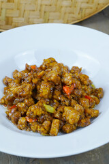 A white plate of Indonesian stir-fried tempeh with soy sauce, chili, and other spices.