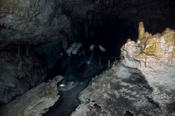 A scuba diver explores a dark, vast cave system with stunning rock formations.