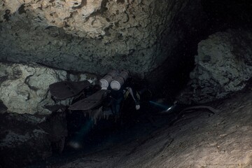 Scuba diver explores a dark, rocky cave underwater.