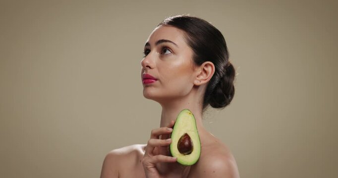 Skincare, glow and woman with avocado in studio for natural, beauty or moisturizing benefits. Cosmetic, happy and female person with fruit for dermatology routine with hydration by brown background.