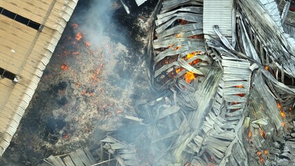 Bird’s eye view of a fire engulfing industrial stacks, with glowing flames piercing twisted, scorched metal layers. Smoke billows upwards, revealing the fire’s destructive force on the facility.  © Punyawee