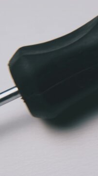 motion past new crosshead screwdriver with red and black handle lying on light surface extreme close view