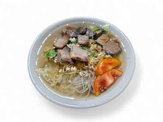 A bowl of traditional Indonesian beef noodle soup served with fresh vegetables and tomato slices on white background, perfect for culinary and food industry visuals