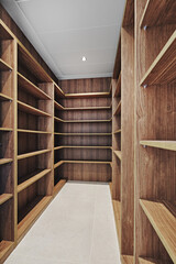 Contemporary walk-in wardrobe with custom wooden shelving and light tiled floor, offering ample storage space for clothes, shoes, and accessories in a minimalistic home design
