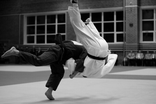 judoka in dark gi is executing high-impact throw on his opponent in white gi