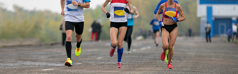 man and two female athletes running marathon on embankment in cool weather
