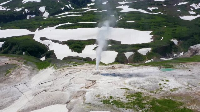 Aerial view of plumes of steam rising from geysers amid a landscape of snow and green vegetation, creating a striking contrast, Kamchatka Krai, Russia.