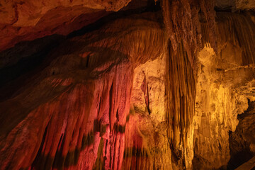 Intricate cave formations rise dramatically from the ground, bathed in warm reds and yellows that highlight their textures