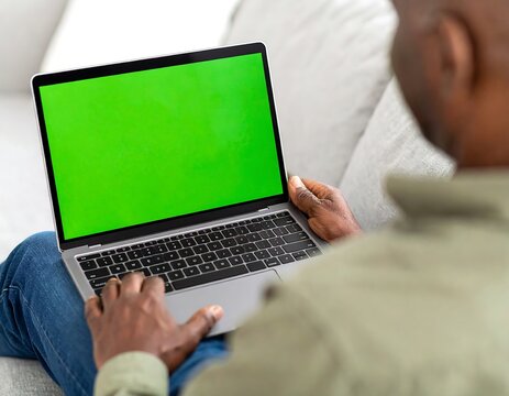 Person sits on a couch using a laptop with a green screen - Powered by Adobe