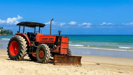 Obraz premium An old red tractor stands on the seashore in Thailand. Preparing the beach for the tourist season. Cleaning and leveling the sand on the beach in Phuket.