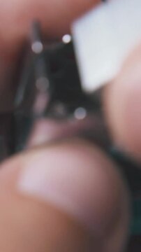 young man opens small turquoise stapler to put in metal clips on dark background extreme close view