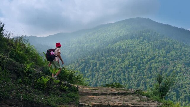 A fit man with a backpack walks down a rocky trail through a beautiful spring forest landscape. The hiker, without trekking poles, follows the downhill path, Madmaheshwar trail, Uttarakhand, India.