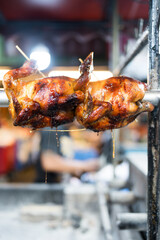 A roasted chicken turning on a spit in a rotisserie oven, showcasing its crispy, golden brown skin at Thai restaurant