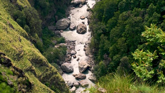 A winding river flows through a lush green valley, surrounded by misty mountains at Buda Madmaheshwar, Rudraprayag, Uttarakhand, India.