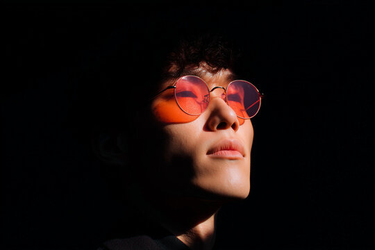 Asian guy standing in darkness wearing glowing neon sunglasses, illuminated with vibrant electric colors, creating a modern, stylish, edgy vibe with strong contrast in an urban, futuristic atmosphere