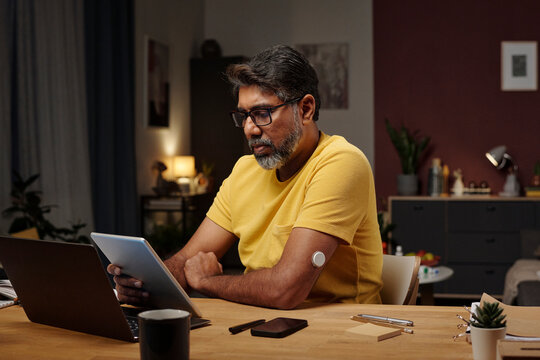 Man using digital device and insulin patch at home office desk