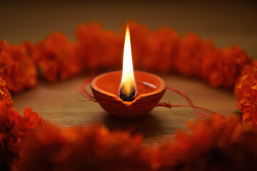 A traditional clay diya lamp with a bright flame, adorned with marigold flowers