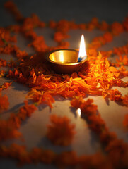 A single lit diya lamp surrounded by marigold flower petals in a circular pattern