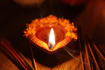 A lit diya lamp with marigold flowers and wisps of smoke from incense sticks