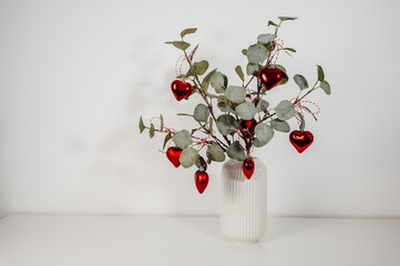 Christmas tree made from eucalyptus branches decorated with red heart ornaments.Festive card with copy space