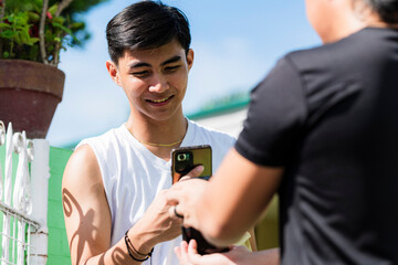 Southeast Asian man smiles as he makes a cashless payment using his phone to scan card reader held by delivery driver