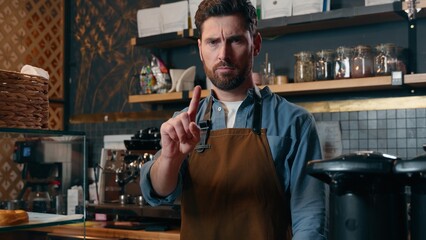 Dissatisfied Caucasian man barista male waving finger warning gesture waiter employee guy looking at camera in cafeteria restaurant small business owner deny forbid prohibition entrepreneur stop sign
