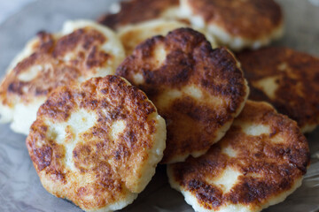 A plate of golden-brown curd cheesecakes stacked neatly. Cheesecakes have a crispy outside and a soft inside