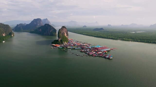Aerial view of Ko Panyi village, nestled against a striking rock formation, with colorful buildings contrasting against the green water, Ko Panyi, Phang Nga, Thailand.