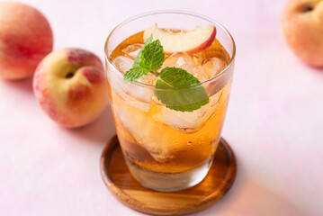 Iced peach tea with fresh sliced peaches and mint leaf in glass on pink background, Summer drink