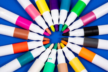 Juego de rotuladores multicolores con las puntas hacia el centro creando un circulo y fondo azul...