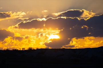 The rays of the setting sun piercing through the clouds above the mountains