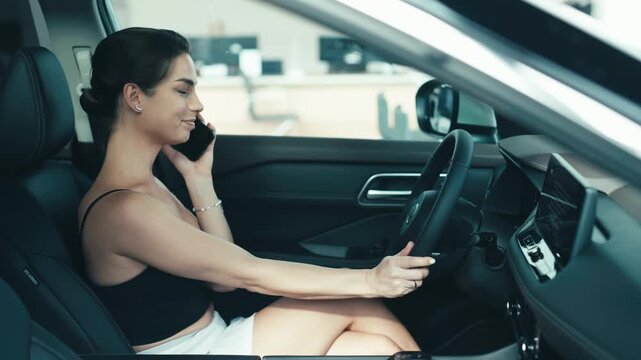 Woman sitting in a car, smiling while talking on her phone, showcasing a modern vehicle interior and a relaxed atmosphere for car buying experience
