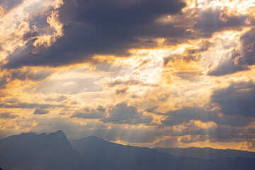 Sunbeams breaking through the clouds at sunset against the backdrop of mountains