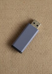 A sleek gray USB drive resting on a textured burlap surface, ideal for secure data storage, A contemporary USB flash drive stands out against a natural, coarse fabric backdrop