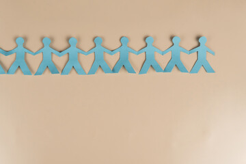 Blue paper cutout of people holding hands in a line on beige background. Symbol of unity, teamwork,...
