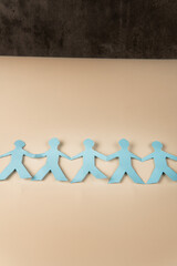 Blue paper cutout of people holding hands in a line on beige background. Symbol of unity, teamwork,...