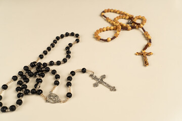 Top view of two rosary prayer beads, one black and one wooden, with crucifixes on a plain cream background. Great for themes of faith, prayer, religion, and Christian symbolism.

