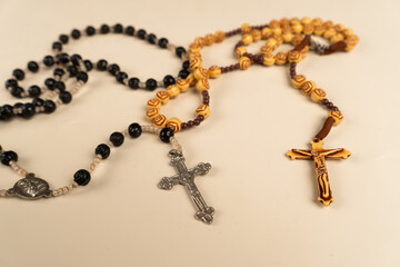 Top view of two rosary prayer beads, one black and one wooden, with crucifixes on a plain cream background. Great for themes of faith, prayer, religion, and Christian symbolism.

