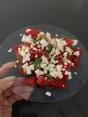 Closeup image of a woman holding a watermelon, feta and basil salad on a glass plate 