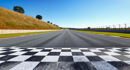 Wide asphalt race track with checkered flag finish line under clear blue sky