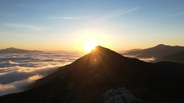 Sunrise over mountain peak cloud inversion below other mountains in the distance clear sky above