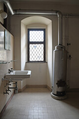 altes Badezimmer mit hellgelben Fliesen, weißem Waschbecken und emailliertem Badeofen